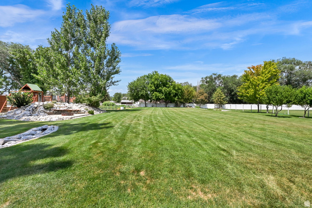 13658 South Fort Street Draper, UT 84020 - Photo 58 of 87 Expansive green lawn with a rock-lined dry creek bed, a built-in fire pit area with stone seating, mature trees providing shade, and a white fence enclosing the perimeter