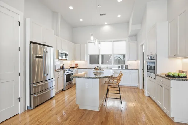 a kitchen with stainless steel appliances a refrigerator a sink dishwasher a stove top oven a refrigerator and white cabinets with wooden floor