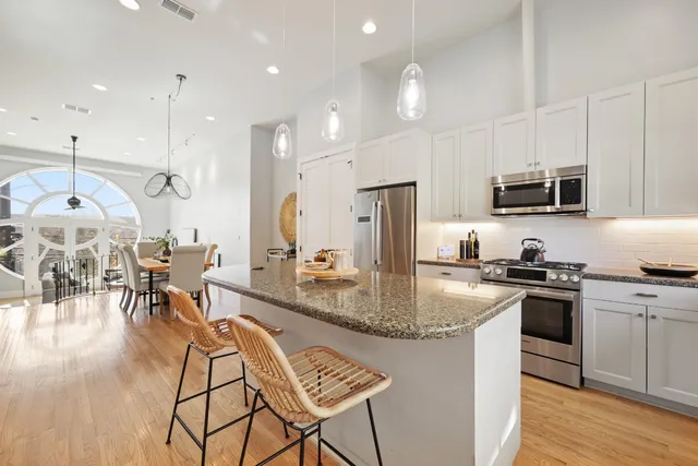 a kitchen with stainless steel appliances granite countertop a stove top oven a refrigerator a sink and chairs