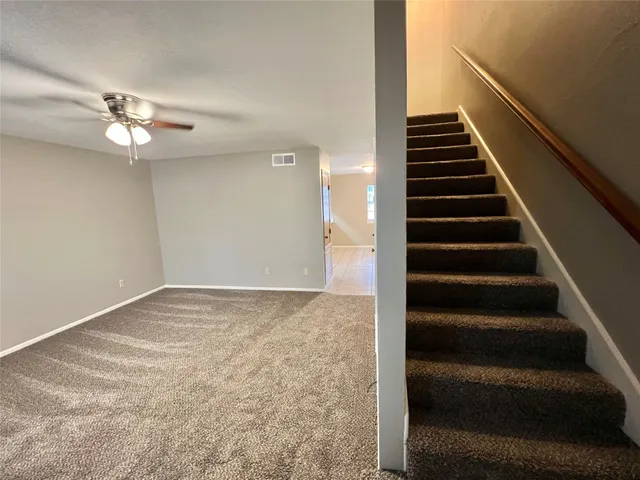 a view of an empty room with stairs and a ceiling fan