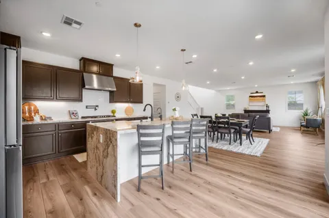 a kitchen with stainless steel appliances kitchen island granite countertop a stove top oven a sink a dining table and chairs with wooden floor