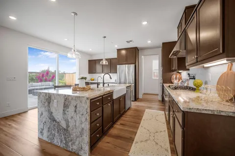 a large kitchen with stainless steel appliances granite countertop plenty wooden cabinets counter space a sink and a wooden floor