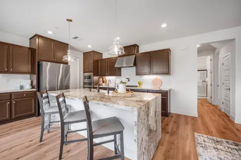 a kitchen with stainless steel appliances a microwave a stove a refrigerator a sink a dining table and chairs with wooden floor