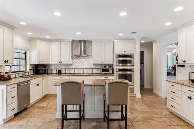 a kitchen with stainless steel appliances granite countertop a stove a sink a refrigerator and white cabinets with wooden floor