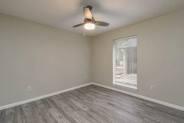 a view of empty room with wooden floor fan and window