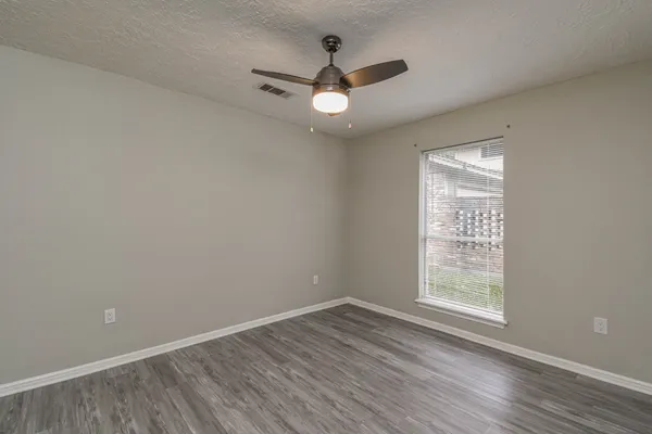 an empty room with wooden floor chandelier fan and windows