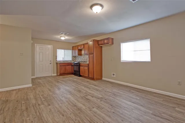 an empty room with wooden floor kitchen view and windows