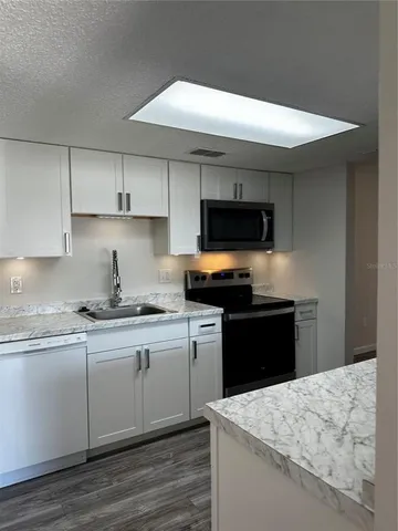 a kitchen with kitchen island granite countertop a sink a stove a microwave and wooden cabinets