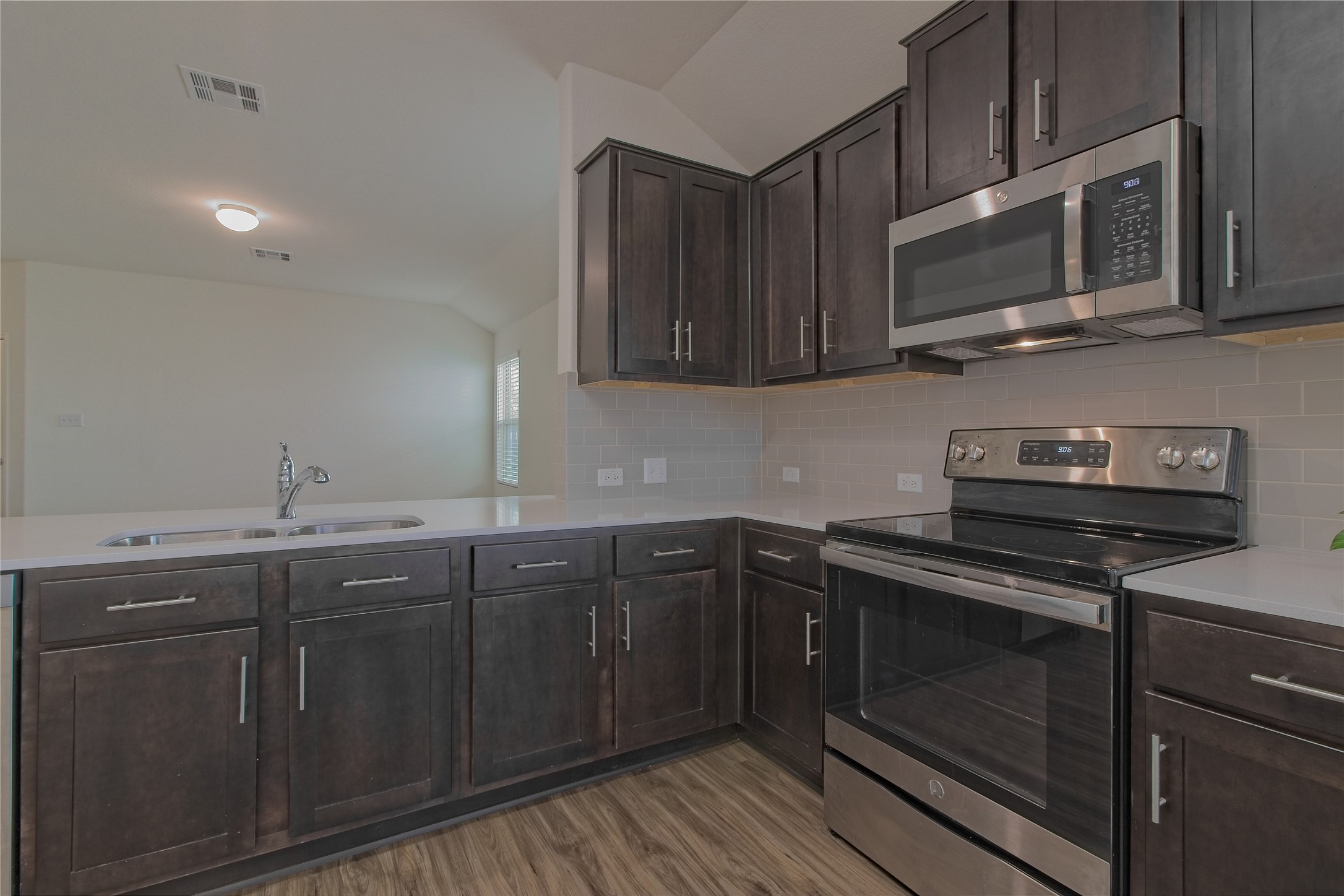 505 Greatest Gift Way Jarrell, TX 76537 - Photo 13 of 30 Kitchen with appliances with stainless steel finishes, dark brown cabinets, lofted ceiling, tasteful backsplash, and light stone counters