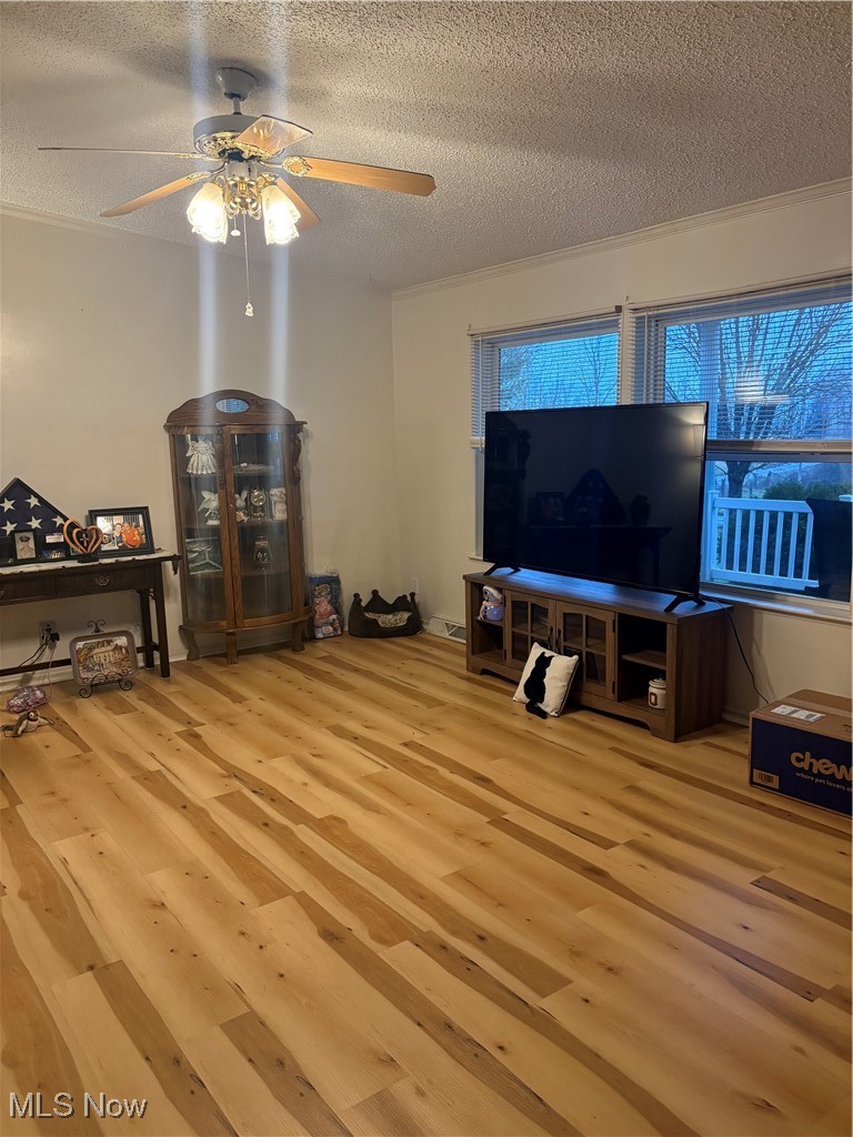 Living room with a textured ceiling, light wood-type flooring, and a ceiling fan
