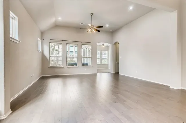 an empty room with wooden floor chandelier fan and windows
