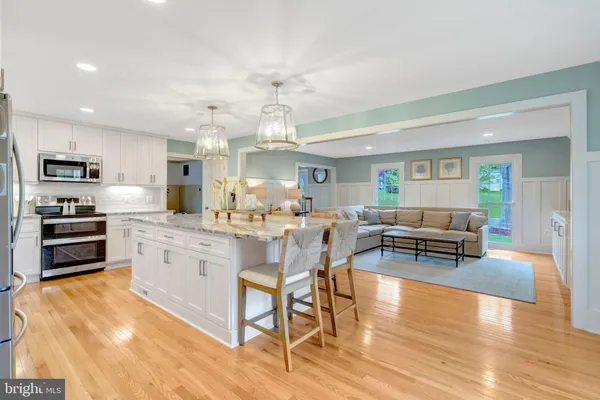 a kitchen with stainless steel appliances kitchen island granite countertop a stove a sink a dining table and chairs with wooden floor