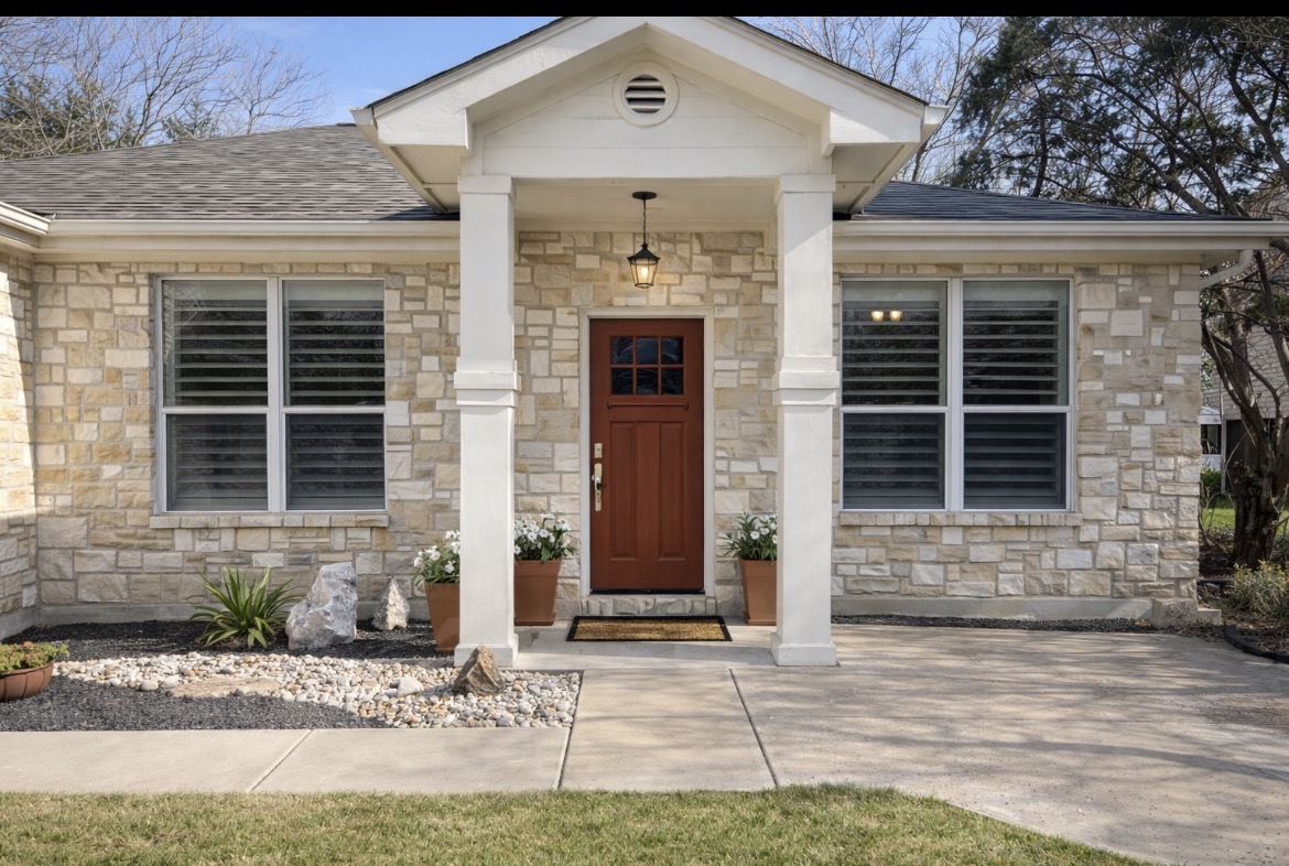 Doorway to property with stone siding, a porch, and roof with shingles
