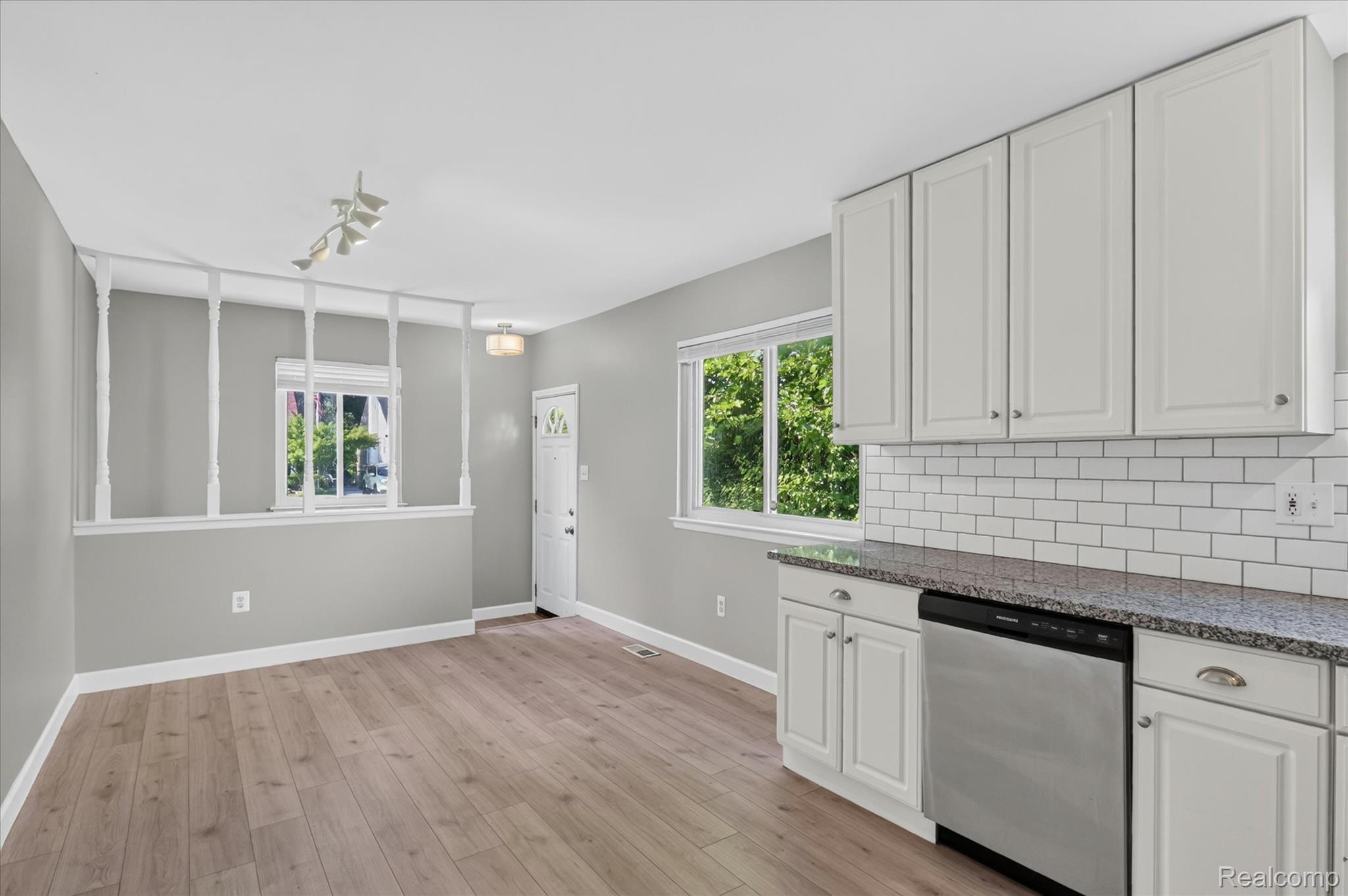 934 Harvard Road Berkley, MI 48072 - Photo 14 of 34 Open-concept living space with wood-finish flooring, white cabinetry, a stainless steel dishwasher, a subway tile backsplash, and stone-finish countertops
