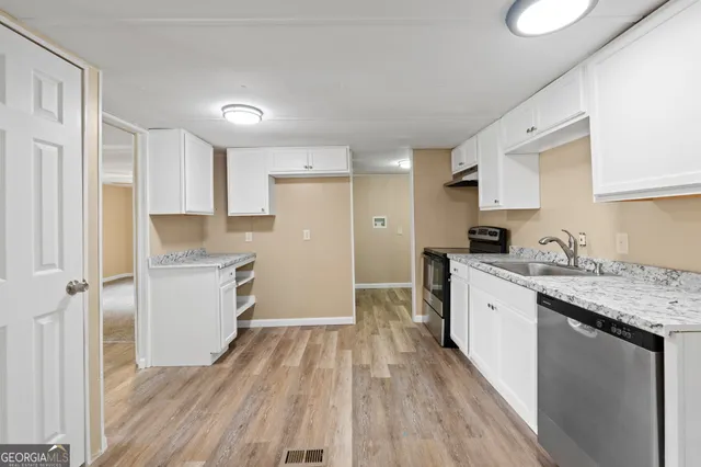 a kitchen with a sink dishwasher stove and white cabinets with wooden floor
