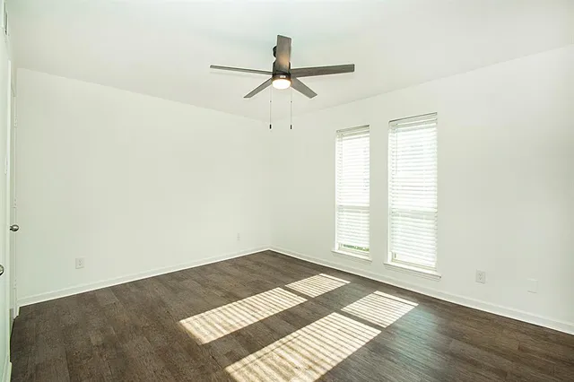 an empty room with wooden floor ceiling fan and windows
