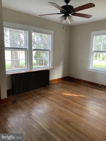 an empty room with wooden floor chandelier fan and windows