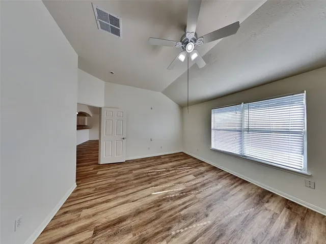 an empty room with wooden floor fan and windows