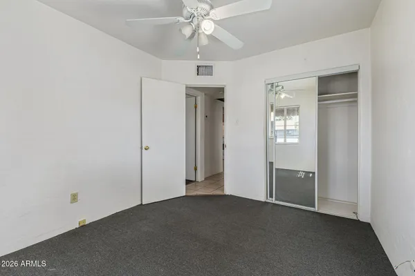 an empty room with chandelier fan and closet area