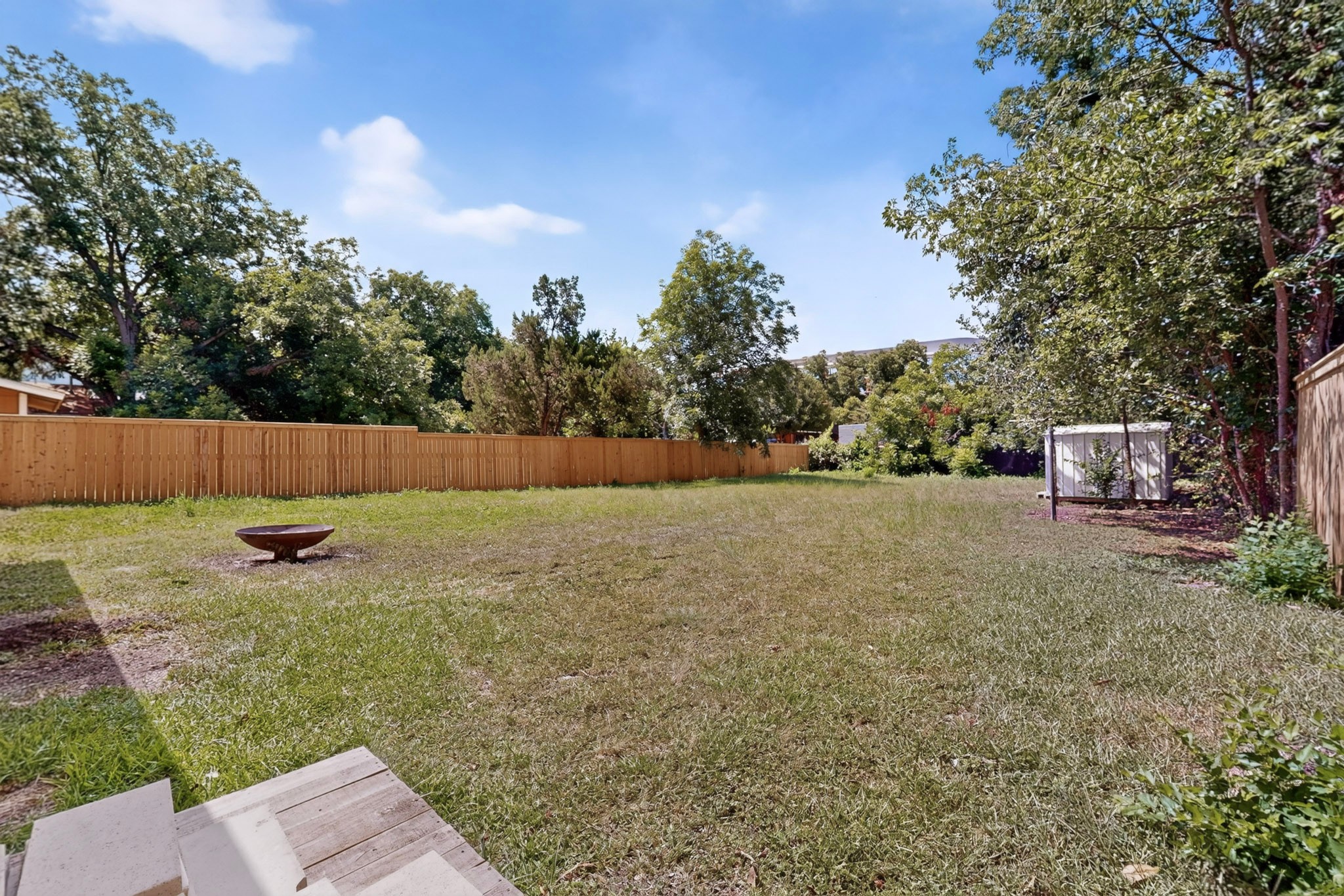 4711 Alf Avenue Austin, TX 78721 - Photo 33 of 34 A spacious backyard enclosed by a tall wooden fence, featuring a fire pit and mature trees.