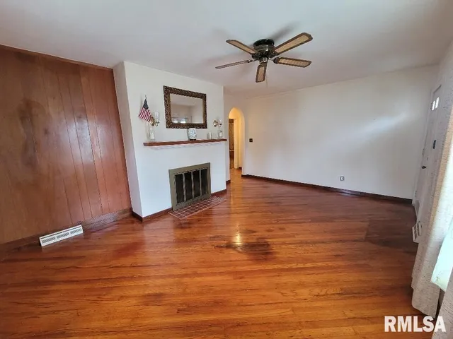a view of a livingroom with a fireplace a ceiling fan and wooden floor