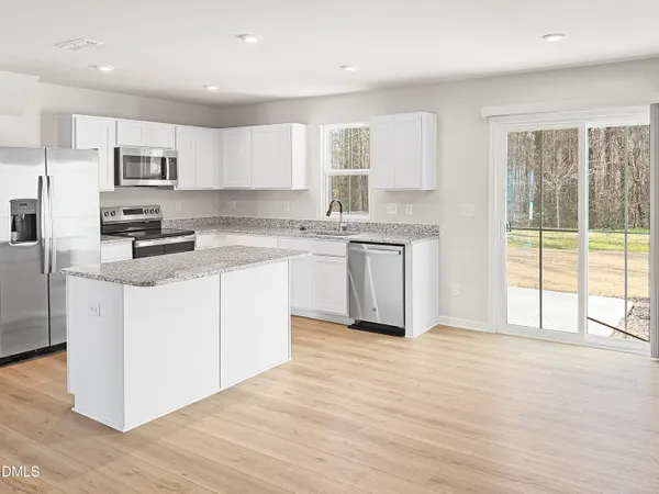 a kitchen with stainless steel appliances granite countertop a stove a sink dishwasher a refrigerator white cabinets and wooden floor next to a window
