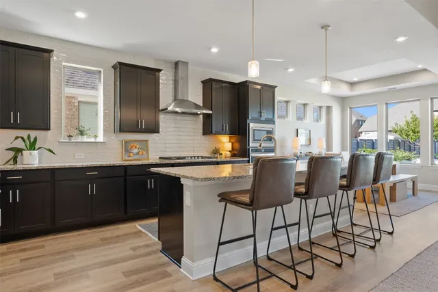 a kitchen with stainless steel appliances granite countertop a refrigerator a stove a sink dishwasher a dining table and chairs with wooden floor