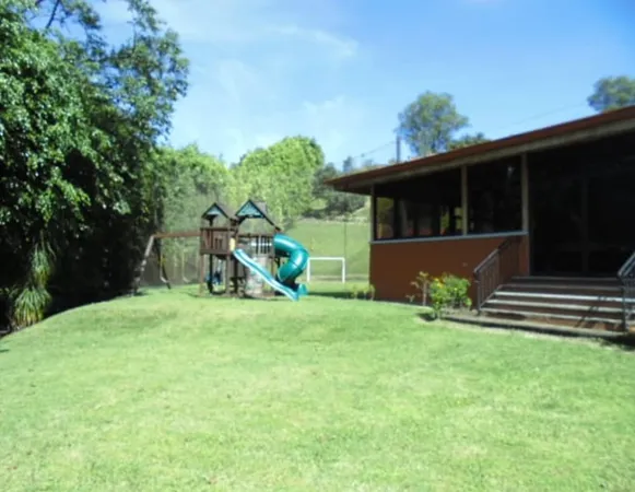 a backyard of a house with table and chairs a barbeque and a large trees