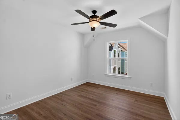 an empty room with wooden floor ceiling fan and windows