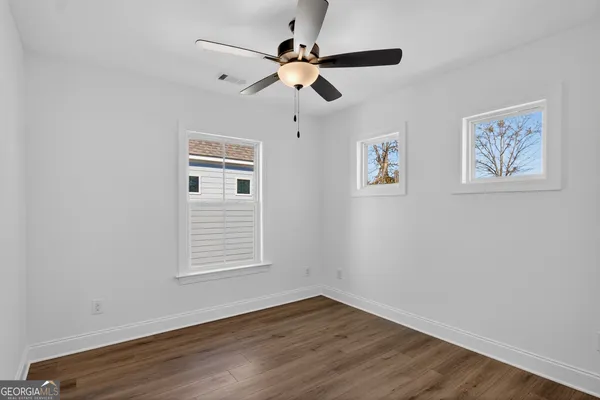 a view of an empty room with wooden floor and a ceiling fan