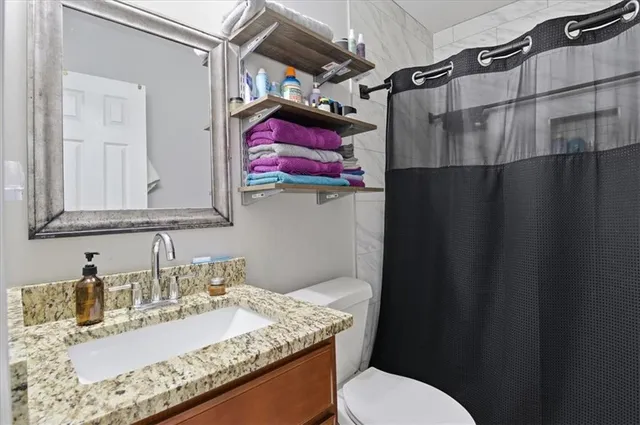 a bathroom with a granite countertop sink vanity mirror and toilet