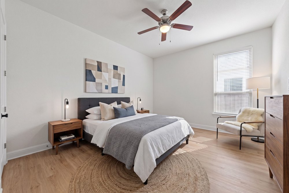Warm wood floors and natural light from a large window define this bedroom.