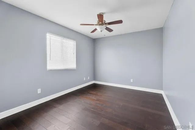 an empty room with wooden floor chandelier fan and windows
