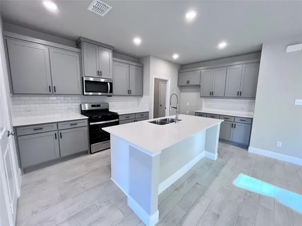 a kitchen with stainless steel appliances a sink a stove a microwave a center island and cabinets