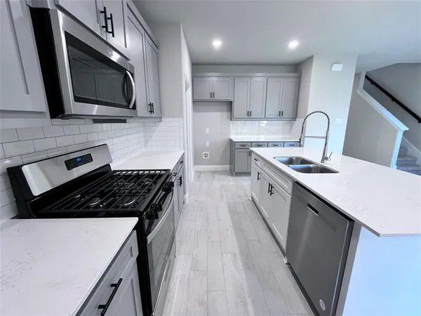 a kitchen with stainless steel appliances a sink dishwasher a stove top oven a refrigerator with grey cabinets and wooden floor