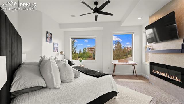 13625 Random Ridge View Colorado Springs, CO 80921 - Photo 17 of 50 Bedroom with light colored carpet, recessed lighting, a glass covered fireplace, and a ceiling fan