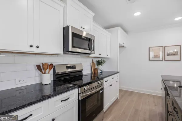 a kitchen with stainless steel appliances granite countertop white cabinets a microwave a sink and a wooden floor