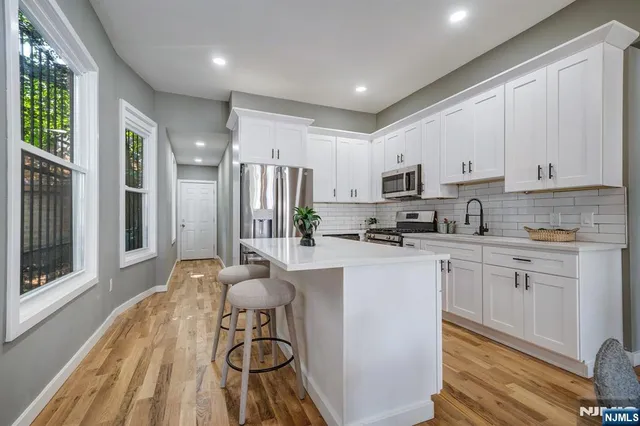 a kitchen with stainless steel appliances granite countertop a refrigerator a stove a sink dishwasher and white cabinets with wooden floor