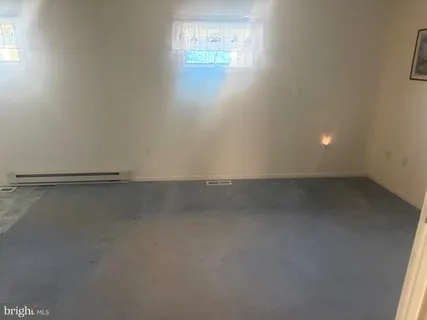 an empty room with windows and view of kitchen