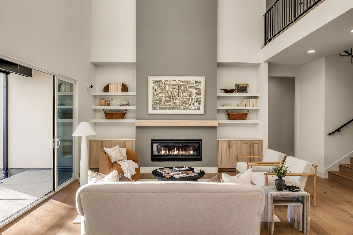 1301 Ruth Avenue Austin, TX 78757 - Photo 5 of 21 Living room with a towering ceiling, built in shelves, a glass covered fireplace, stairway, and wood finished floors
