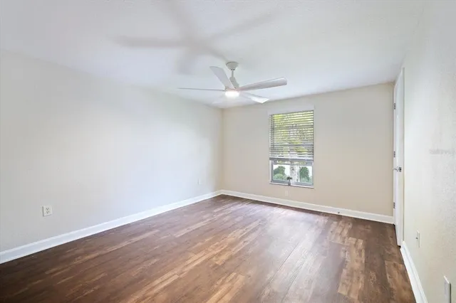 an empty room with wooden floor chandelier fan and windows