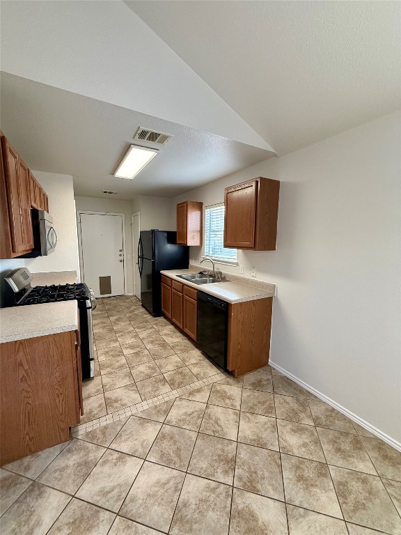 18304 Belfry Pass Manor, TX 78653 - Photo 14 of 26 Kitchen with black appliances, light countertops, brown cabinetry, light tile patterned floors, and vaulted ceiling