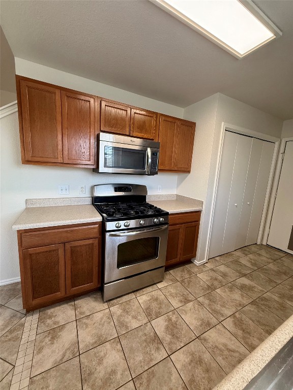 18304 Belfry Pass Manor, TX 78653 - Photo 15 of 26 Kitchen featuring stainless steel appliances, brown cabinets, light countertops, and light tile patterned floors