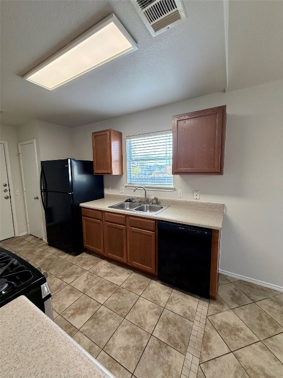 18304 Belfry Pass Manor, TX 78653 - Photo 16 of 26 Kitchen featuring brown cabinets, black appliances, light countertops, light tile patterned floors, and a textured ceiling