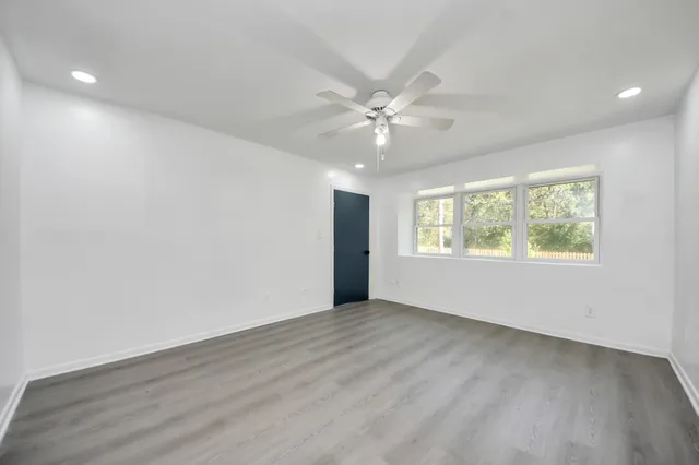 an empty room with wooden floor chandelier fan and windows