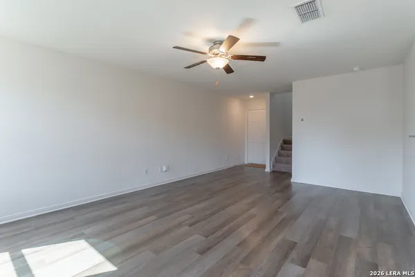 an empty room with wooden floor fan and windows