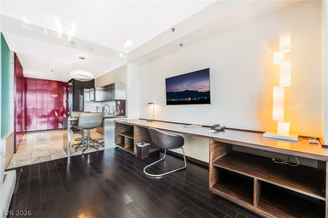 4381 West Flamingo Road, Unit 18305 Las Vegas, NV 89103 - Photo 17 of 19 Rich hardwood flooring complements a sleek kitchen with modern appliances and an integrated desk area.