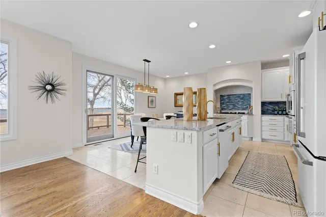 a large white kitchen with granite countertop a large counter top a sink appliances and cabinets