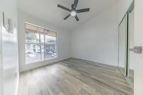 an empty room with wooden floor fan and windows