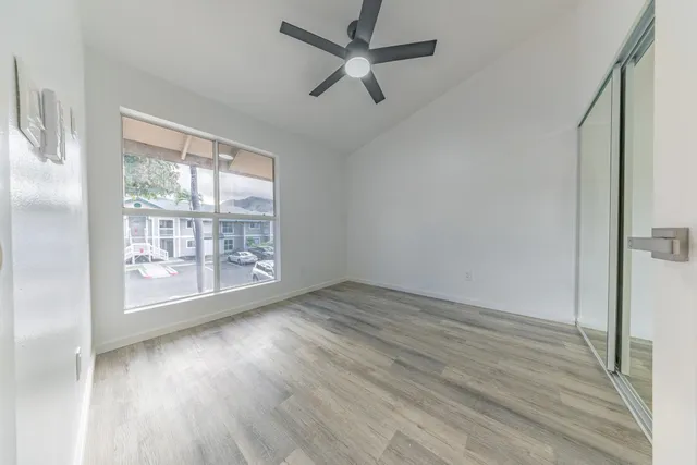 an empty room with wooden floor fan and windows